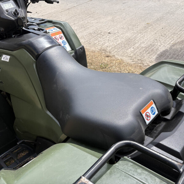 Close-up view of a green Honda ATV seat, handlebars, and warning sticker panels on the body.