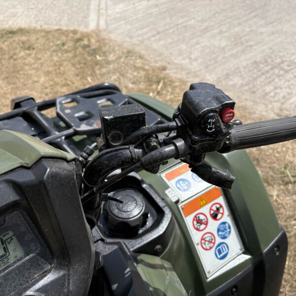 Close-up of an ATV/quad bike handlebar with grip, ignition area, and red 4WD switch visible beside warning labels.