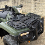Front view of a green ATV with a lit headlight, cargo rack, and stone wall in the background.','Close-up of the front of a green ATV showing the headlight, handlebars, and rugged bumper.','ATV parked on dry grass beside a stone wall, displaying the front grill and rack.','Green all-terrain vehicle with a front bumper and rack, visible tire treads and dirt.']}}Oops quotes formatting. Need JSON array properly. Let's fix.