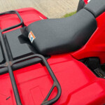 Close-up of a red motorcycle/scooter with a black metal rear rack and a small sticker on the body surface.