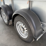 Dual-axle trailer wheel and black plastic fender guards on a silver trailer side wall.