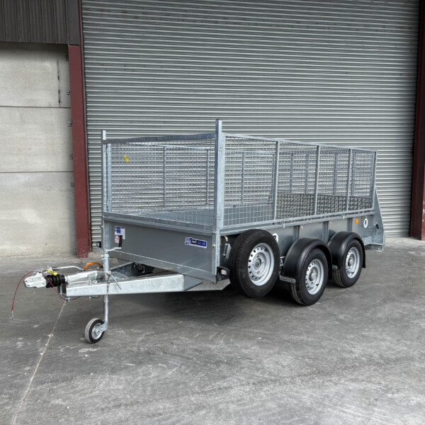 Metal utility trailer with mesh sides and dual axles parked in front of a large corrugated metal roll-up door at an industrial site a yellow door on the right side faintly visible