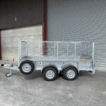 Silver utility trailer with mesh sides and dual axles parked indoors in front of a corrugated metal shutter.
