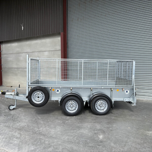 Silver utility trailer with mesh sides and dual axles parked indoors in front of a corrugated metal shutter.
