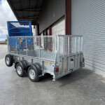 Flatbed trailer with a blue metal cage cargo container parked beside a corrugated warehouse with a large roller door.