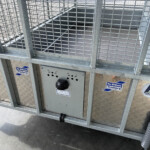 Rear of a galvanized metal trailer with grid fencing and diamond-plate base, showing several company stickers (Russell's Trailers).