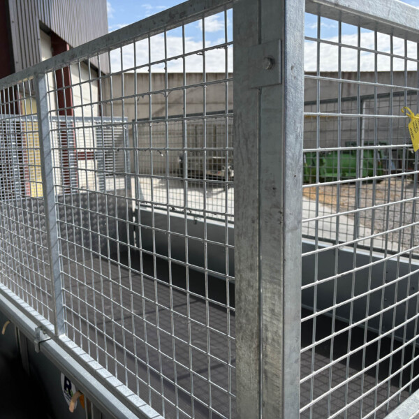 Industrial galvanized wire fence panels forming a gate at an outdoor warehouse area with a yellow tag attached to the mesh.