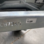 Close-up of a gray metal surface with embossed digits and a white barcode label reading GH106HD on the edge of a frame.