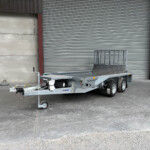Industrial yard scene with a utility trailer in front of a large gray corrugated metal roller shutter; a yellow door is on the right.