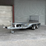 Utility trailer with hitch and dual axles parked in an industrial loading area in front of a large corrugated metal door.