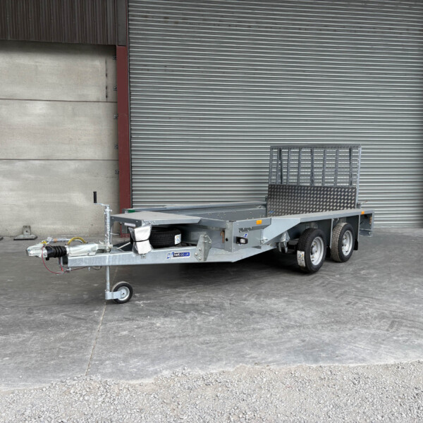 Utility trailer with hitch and dual axles parked in an industrial loading area in front of a large corrugated metal door.