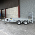 Industrial loading area with a blue trailer on the left and a silver trailer bed inside a warehouse with a corrugated metal wall and a large rolled door on the right