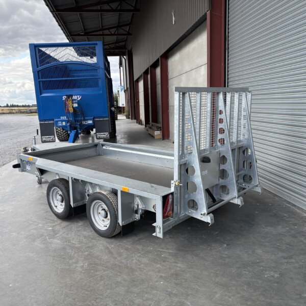 Blue trailer parked beside an industrial building with a corrugated metal roll-up door and metal framework above it.