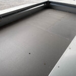 Industrial metal loading platform with a textured black non-slip surface and a silver edge, small leaves scattered nearby.