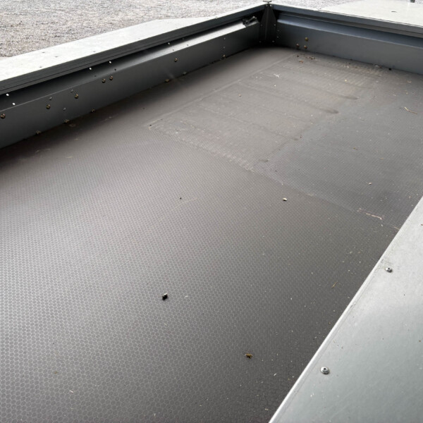 Industrial metal loading platform with a textured black non-slip surface and a silver edge, small leaves scattered nearby.