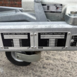 Close-up of a silver trailer body with plaques reading IFOR WILLIAMS TRAILERS LTD and weight specs, wheel visible beneath.