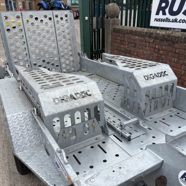 Close-up of a rugged galvanized trailer step with perforated treads and side handles, parked beside a brick wall.