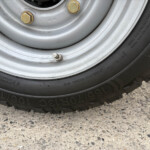 Close-up of a car wheel showing a gray rim, gold lug nuts, and a tire with a valve stem visible.