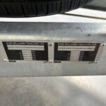 Close-up of a trailer frame with weight-rating plates reading 'IFOR WILLIAMS TRAILERS LTD' beneath the tire above.