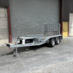 Industrial trailer parked near a warehouse with large corrugated metal roller door behind it at a loading area.