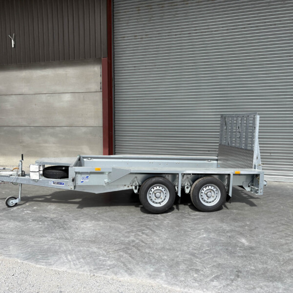 Industrial trailer with a spare tire and towing hitch parked on a concrete lot beside a large corrugated metal wall and roll-up door.