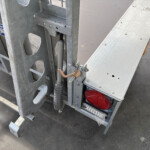 Close-up of a galvanized scaffold frame with a hydraulic cylinder and hose, plus a red rear light on the platform area.