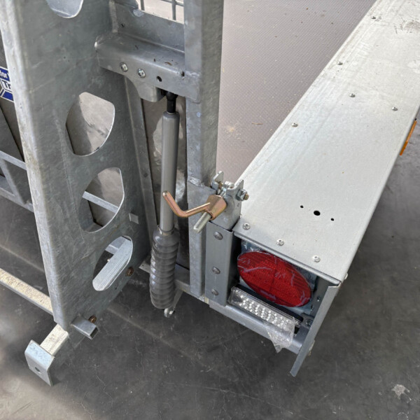 Close-up of a galvanized scaffold frame with a hydraulic cylinder and hose, plus a red rear light on the platform area.