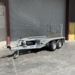 Industrial loading dock with a closed corrugated metal roll-up door, a yellow door to the right, and a utility trailer in the foreground.