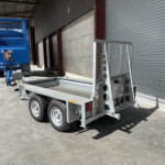 Blue industrial trailer with mesh sides parked beside a gray concrete loading dock under a metal awning.