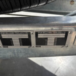 Close-up of two Ifor Williams Trailers identification plates on a metal chassis, with a tire visible above them.