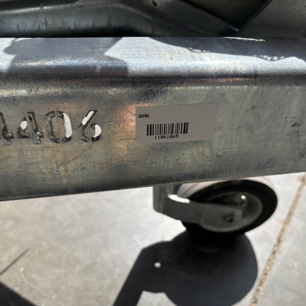 Industrial metal surface with stamped numbers and a GX84 barcode sticker, shadows of a person cast nearby, and a wheel visible below.