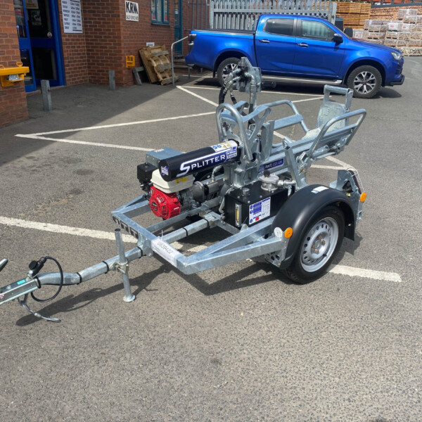 Metal boat trailer with engine and hitch in a parking lot near a brick building and a blue pickup truck in the background.