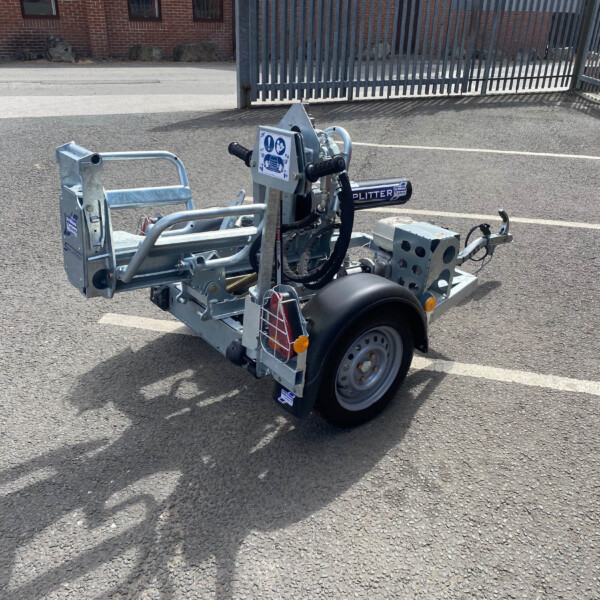 Trailer hitch and utility trailer frame in a parking lot, with a metal gate in the background and a brick building.
