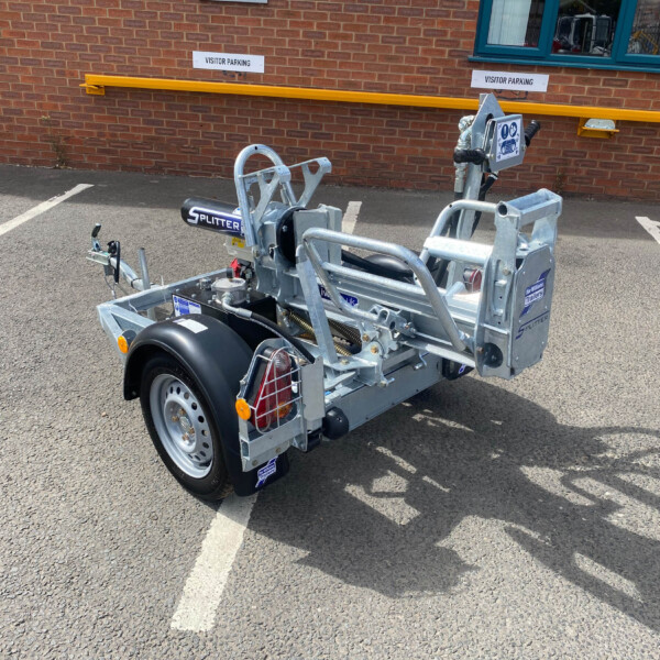 Metal trailer in a parking lot beside a brick building, with a bright yellow safety rail and 'Visitor Parking' signs in the background
