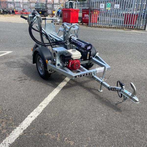 Trailer-mounted equipment with hydraulic hoses and a small gas engine in a parking lot scene.