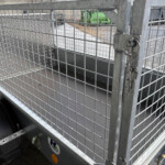 Metal wire cage with a padlock securing the gate; industrial yard and equipment visible in the background.