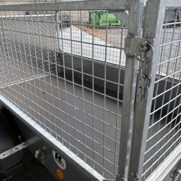 Metal wire cage with a padlock securing the gate; industrial yard and equipment visible in the background.