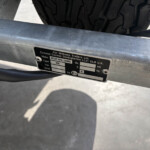 Close-up of a metal trailer frame with a black ID plate and a tire in the background.