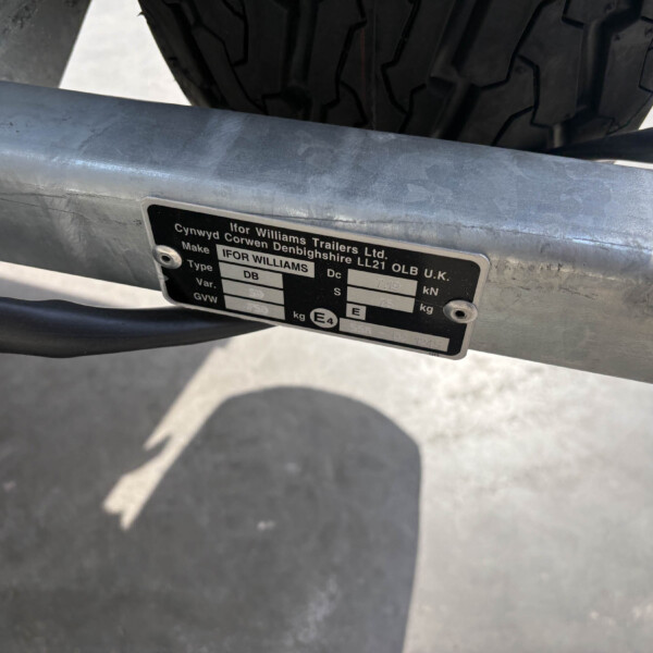 Close-up of a metal trailer frame with a black ID plate and a tire in the background.