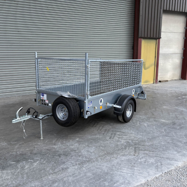 Metal utility trailer with mesh sides and hitch, parked on a concrete floor in front of a large gray industrial roller door.