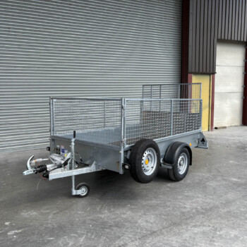 Dual-axle metal utility trailer with mesh sides parked in front of a gray corrugated roll-up door.