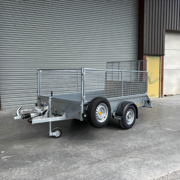Metal utility trailer with mesh sides in front of a large gray corrugated roll-up door in an industrial loading area.