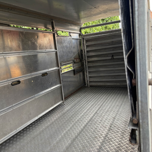 Interior view of an empty metal trailer with diamond-plate floor and side panels, open back doors revealing outside street.