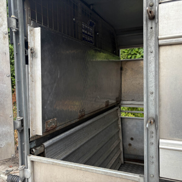Open metal truck trailer with empty cargo hold and rear doors swung wide, showing metallic walls and floor.