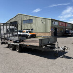 Industrial building with corrugated metal walls, loading dock, and several company vans in a fenced yard.