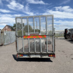 Rear view of a metal mesh gate on a parked trailer in an industrial yard under a blue sky with scattered clouds