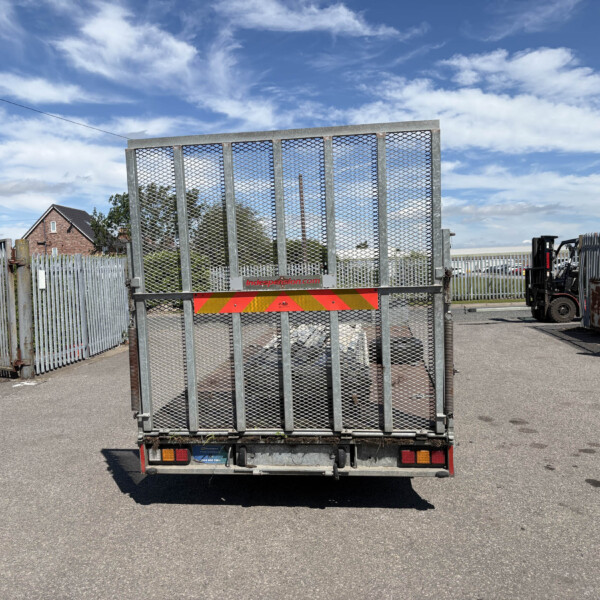 Rear view of a metal mesh gate on a parked trailer in an industrial yard under a blue sky with scattered clouds