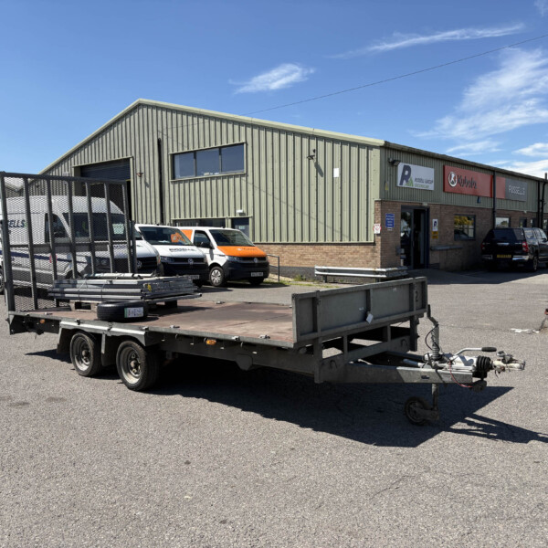 Industrial building with corrugated metal walls, loading dock, and several company vans in a fenced yard.