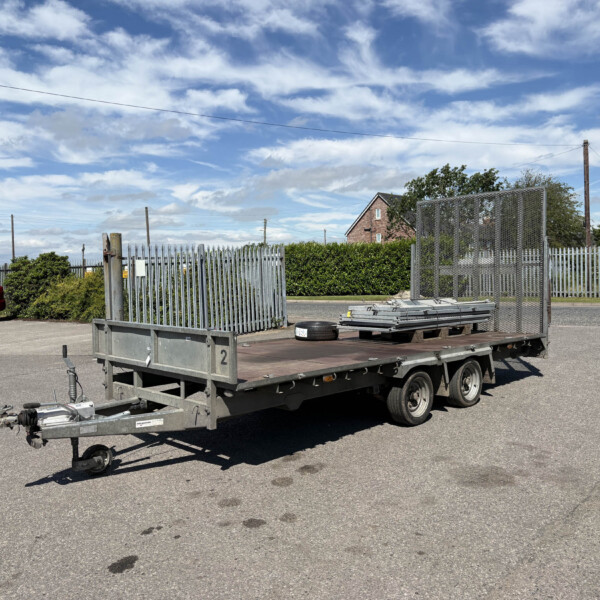 Flatbed trailer with metal mesh sides parked in an empty lot, blue sky and scattered clouds overhead, and a red car in the background.