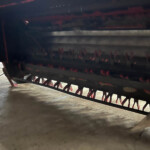 Close-up of a red farming implement’s tines and frame under dim light.